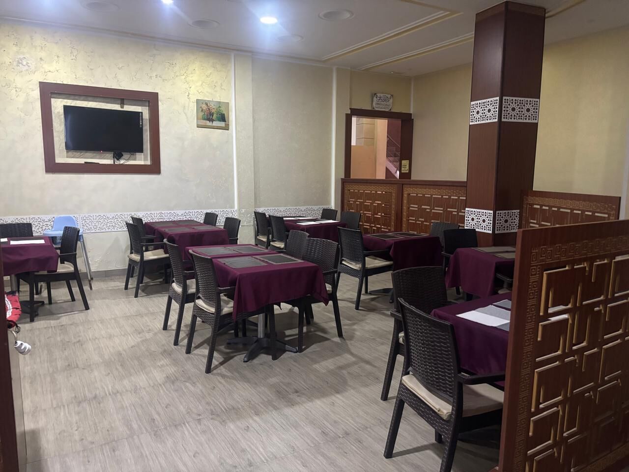 Un restaurant avec des tables et des chaises, un téléviseur fixé au mur et un élément de décoration servant de séparation.