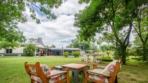 Un área de estar al aire libre con muebles de madera y una mesa, rodeada de césped y árboles.