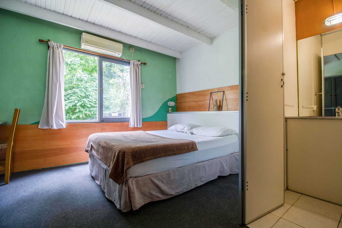 Una camera da letto con un letto, una finestra con tende, una testiera in legno e un comodino.