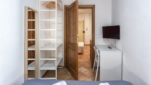 A bedroom with a bed, a desk, a TV, a wardrobe, and a bathroom visible through an open door. - Zannoni Apartments (Florence)