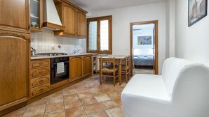 A compact kitchen with wooden cabinets, a stove, and a dining area with a white sofa. - Zannoni Apartments (Florence)