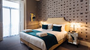 Ein Hotelzimmer mit Bett, Nachttisch, Spiegel, Wand mit Schmetterlingsmuster und Fenster mit Vorhängen.