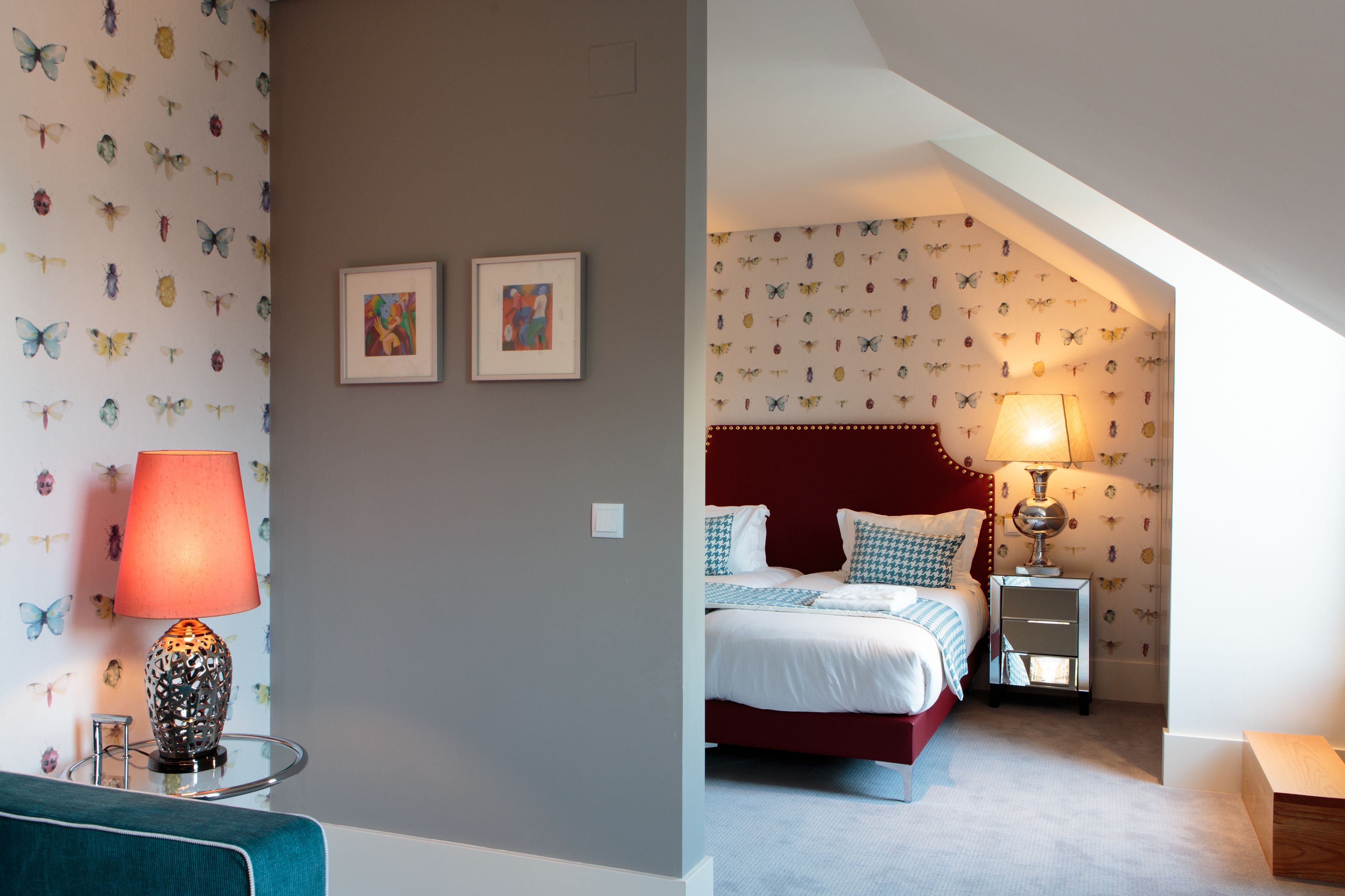 A bedroom with a red headboard, a bed with white bedding, a nightstand with a lamp, and butterfly-patterned wallpaper.
