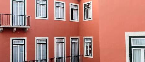 Ein Gebäude mit mehreren Fenstern und Balkonen, das eine rote Fassade und weiße Fensterrahmen aufweist.
