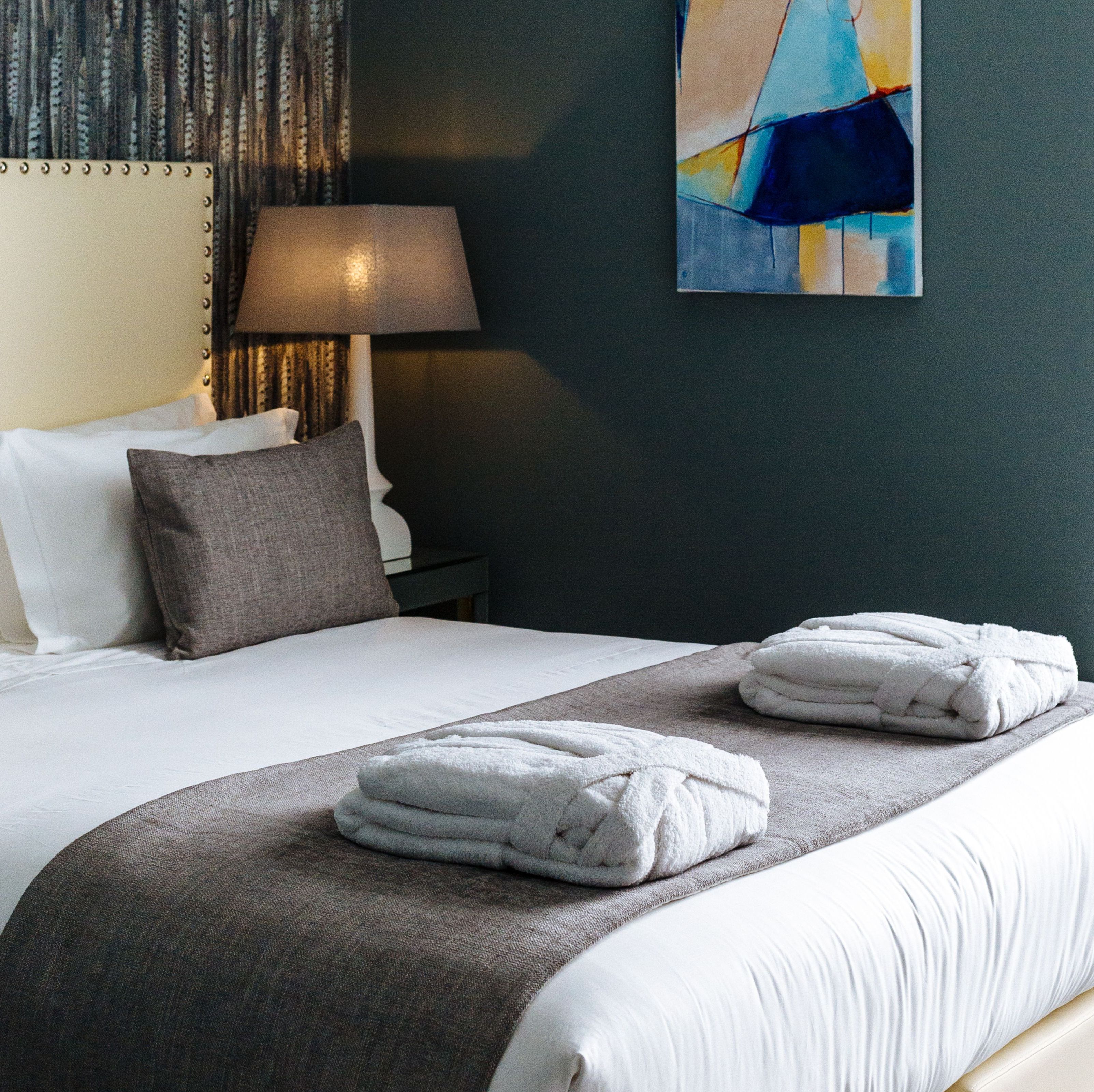 Una cama bien hecha con sábanas blancas, un plaid gris y dos toallas dobladas.