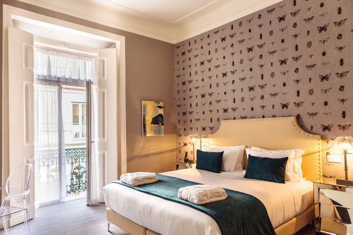 Een hotelkamer met een bed, nachtkastje, stoel en uitzicht op het balkon.
