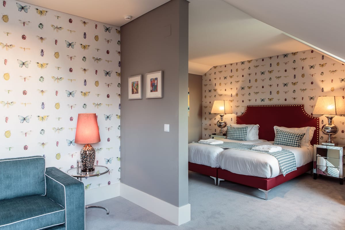 Een slaapkamer met een rode hoofdbord, twee nachtkastjes met lampen, een bed met wit beddengoed en een blauwe fauteuil.