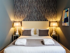 A neatly made bed with white and gray linens, two bedside lamps, and a patterned headboard.