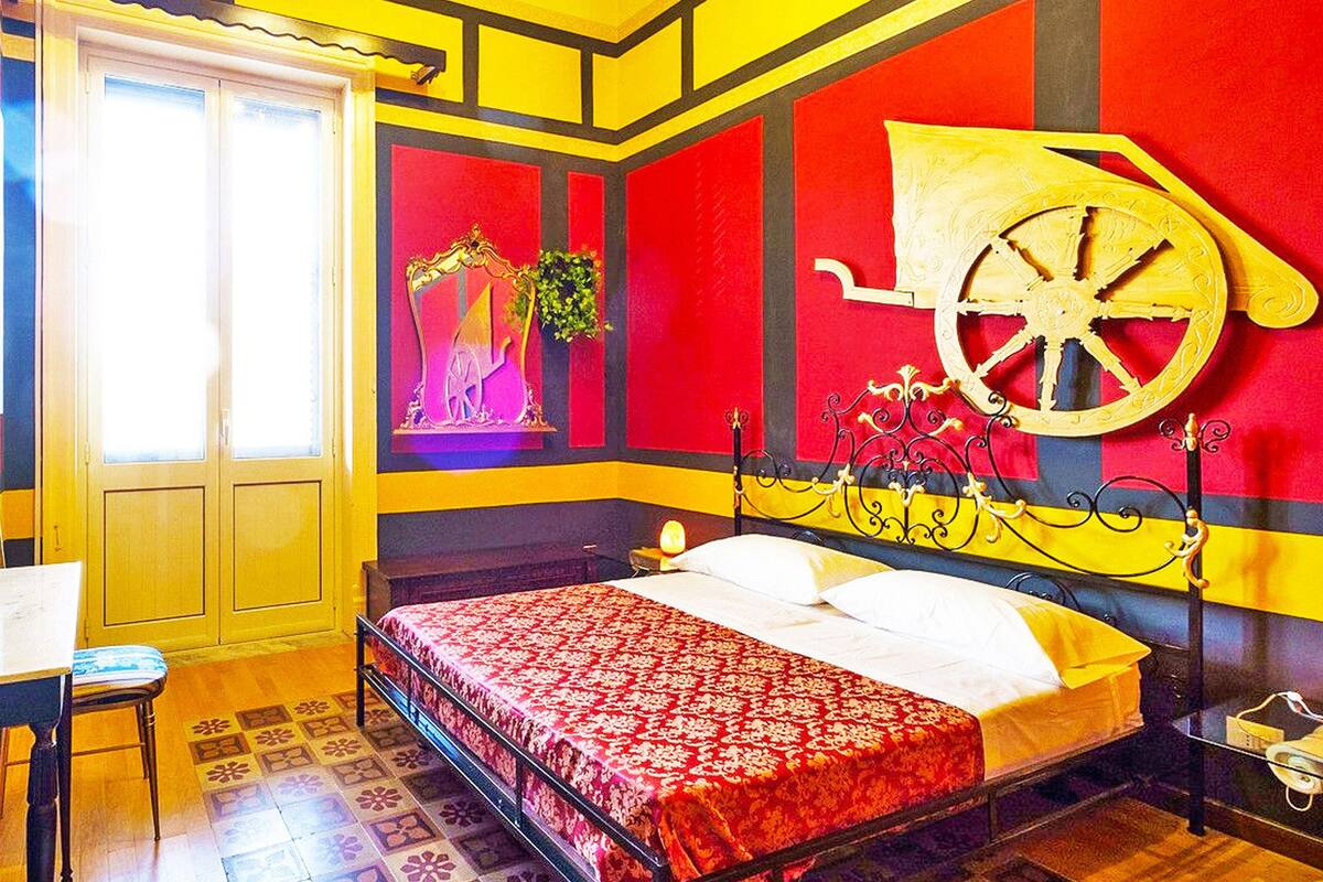 Une chambre à coucher avec un lit, une table de chevet, une chaise et une fenêtre avec des rideaux.