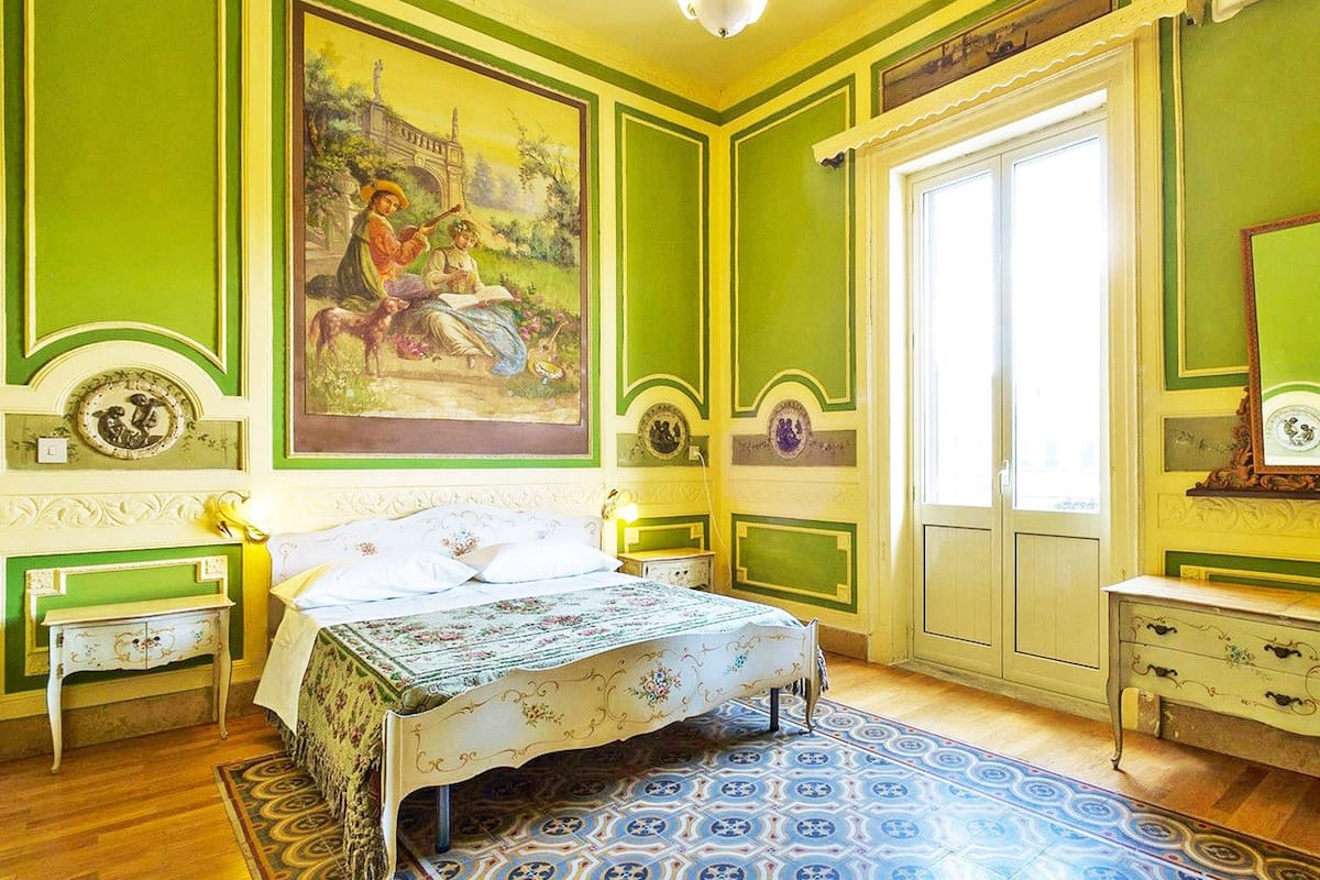 Une pièce avec un lit, un grand tableau, une fenêtre et une commode.