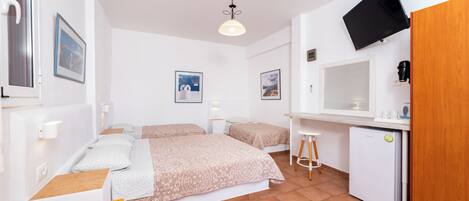 Habitación compacta con dos camas, una kitchenette pequeña, un televisor montado en la pared y una puerta de madera.