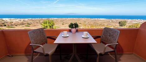 A balcony with two chairs and a table, overlooking a coastal landscape.