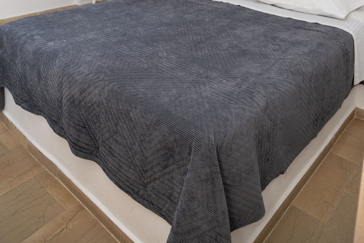 Ein Schlafzimmer mit Bett, Schreibtisch, Stuhl, einer Hängelampe und einem Wandspiegel.