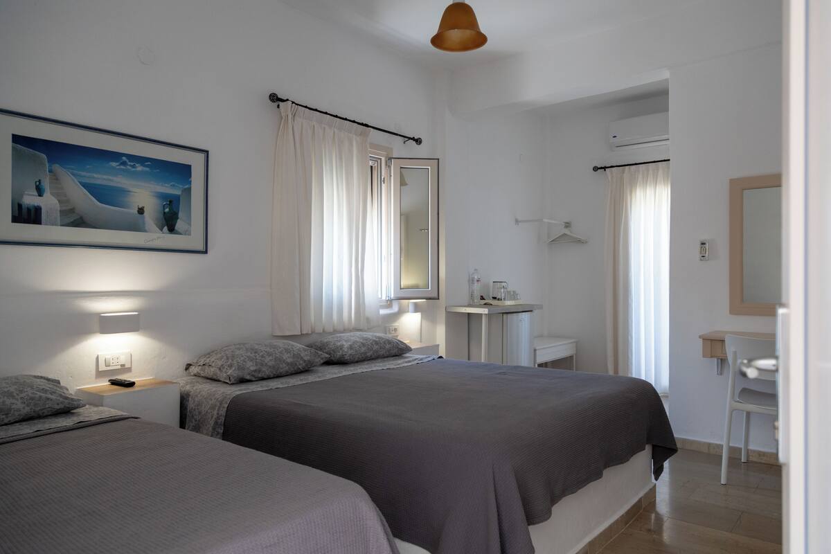 Ein Hotelzimmer mit zwei Betten, einem Nachttisch, einem kleinen Schreibtisch, einem Spiegel und einem Bild an der Wand.