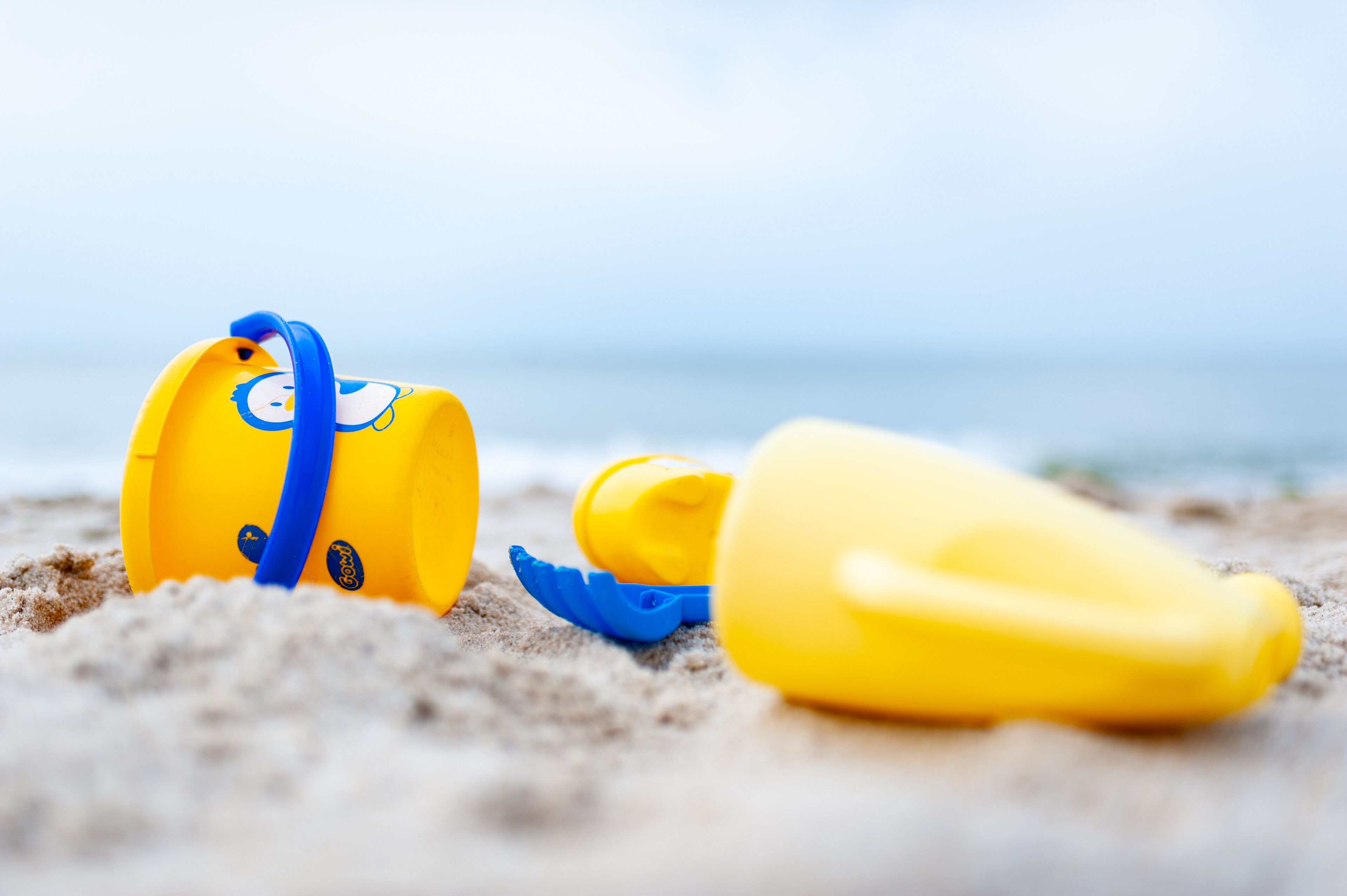Escena de playa con un cubo amarillo y una pala azul sobre la arena.