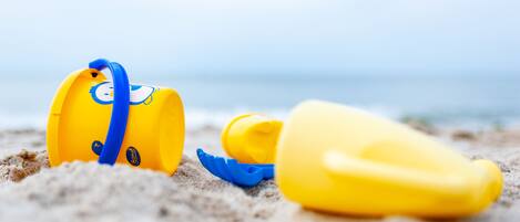 Escena de playa con un cubo amarillo y una pala azul sobre la arena.