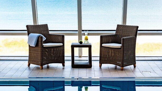 Two wicker chairs facing a pool with a view of the sea.