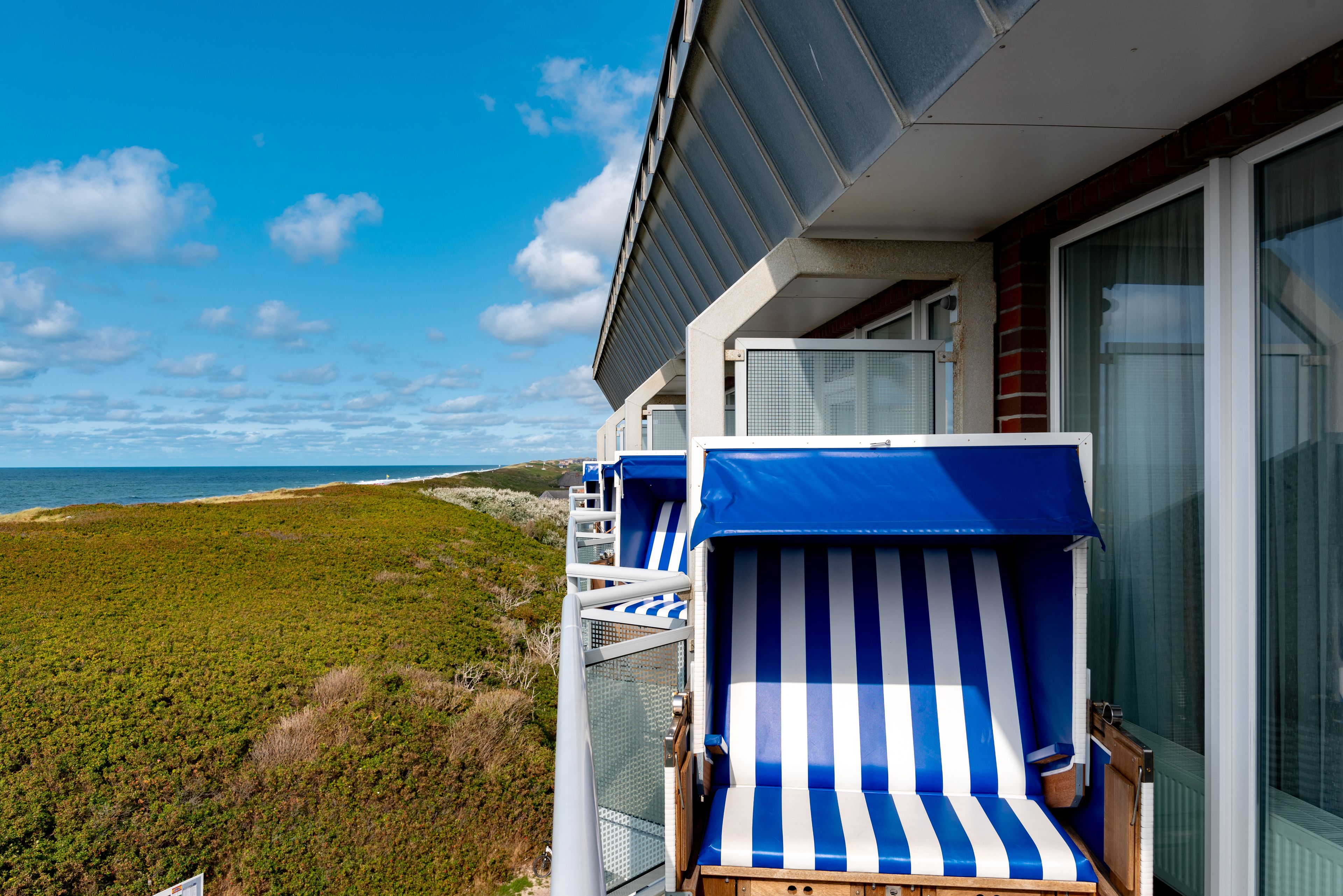 Un balcone con due poltrone a righe blu e bianche, una ringhiera in vetro e vista sulla spiaggia e sull'oceano.