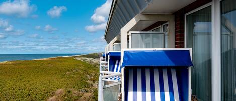 Un balcone con due poltrone a righe blu e bianche, una ringhiera in vetro e vista sulla spiaggia e sull'oceano.