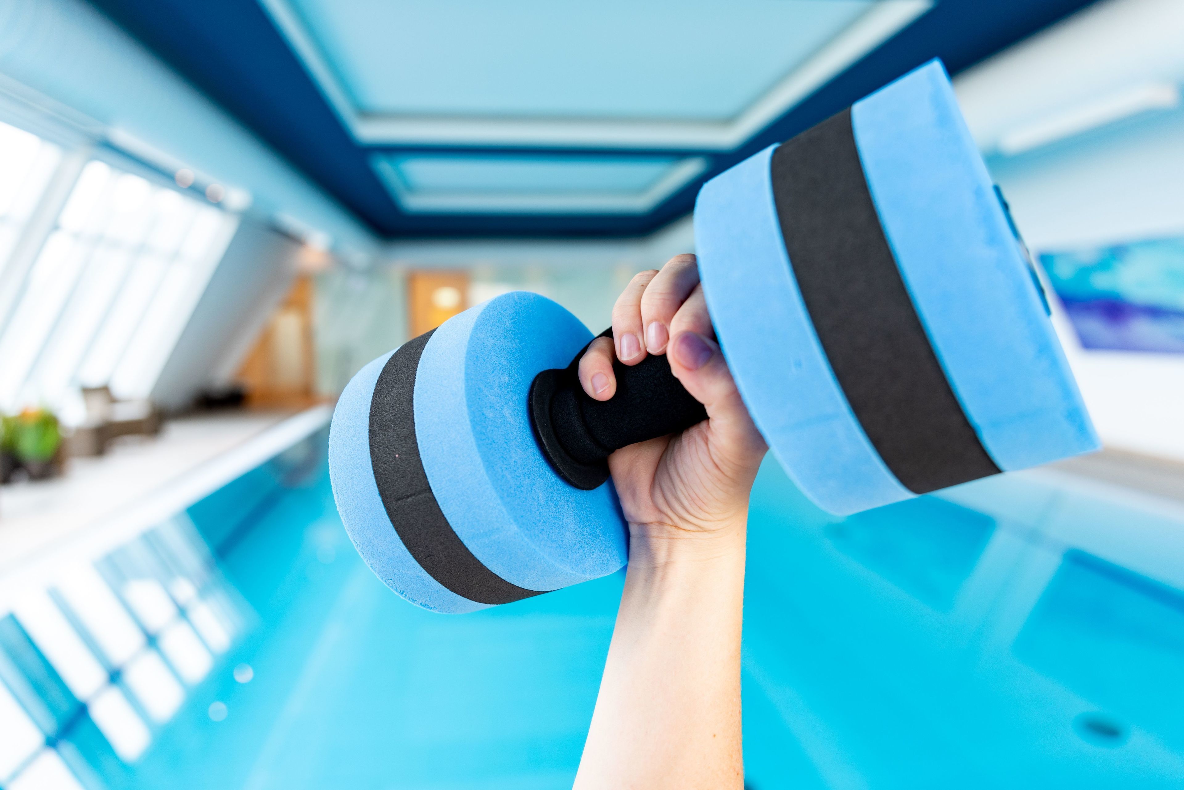A hand holding a blue and black dumbbell near a swimming pool.