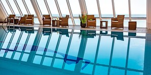 An indoor swimming pool with wicker furniture and potted plants, large windows with a view of the sea. - Wyn. Strandhotel Sylt (Sylt)