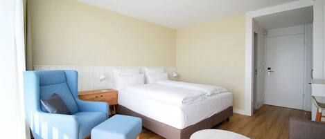 Een moderne hotelkamer met een groot bed, een blauwe fauteuil, een klein voetenbankje en een ronde tafel.