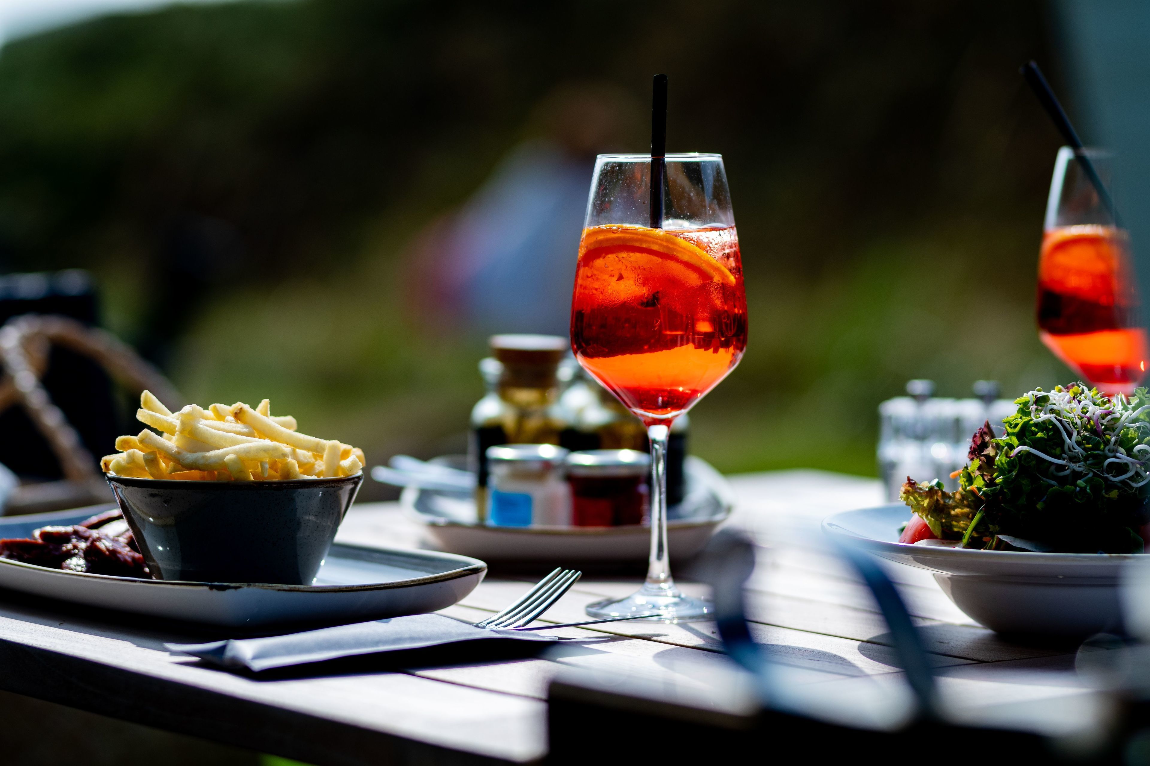 Ein Tisch, gedeckt mit einem Glas roter Flüssigkeit, einer Schüssel Pommes und einem Salat.