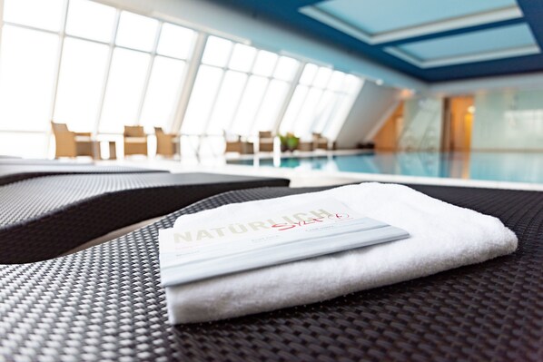 A poolside area with a towel and a card, a seating area with chairs, and a view of the pool. - Wyn. Strandhotel Sylt (Sylt)