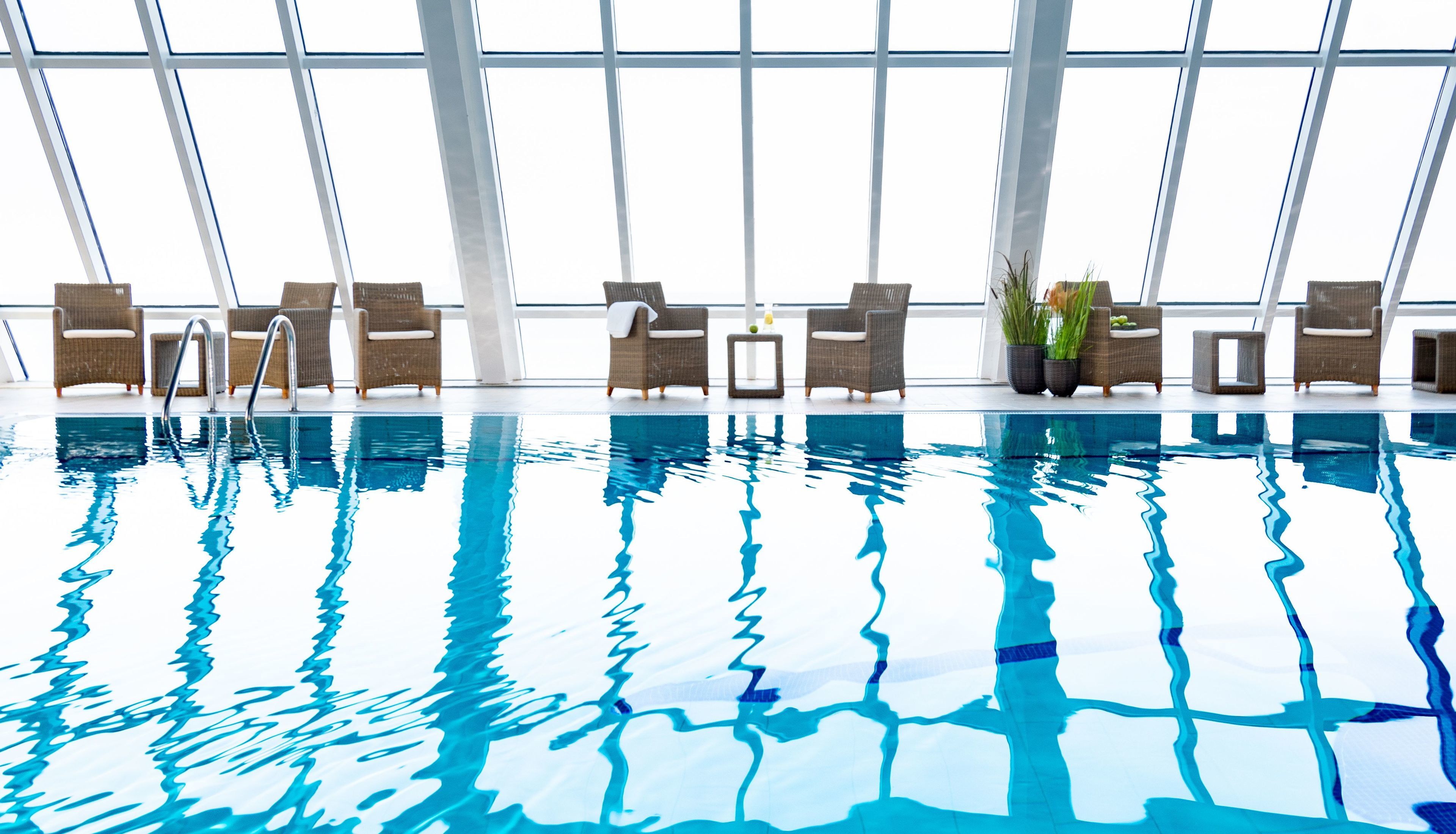 An indoor swimming pool with clear blue water, surrounded by wicker lounge chairs and potted plants.