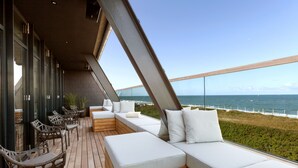 A balcony with wooden flooring, white cushioned seating, wicker chairs, and a view of the ocean.