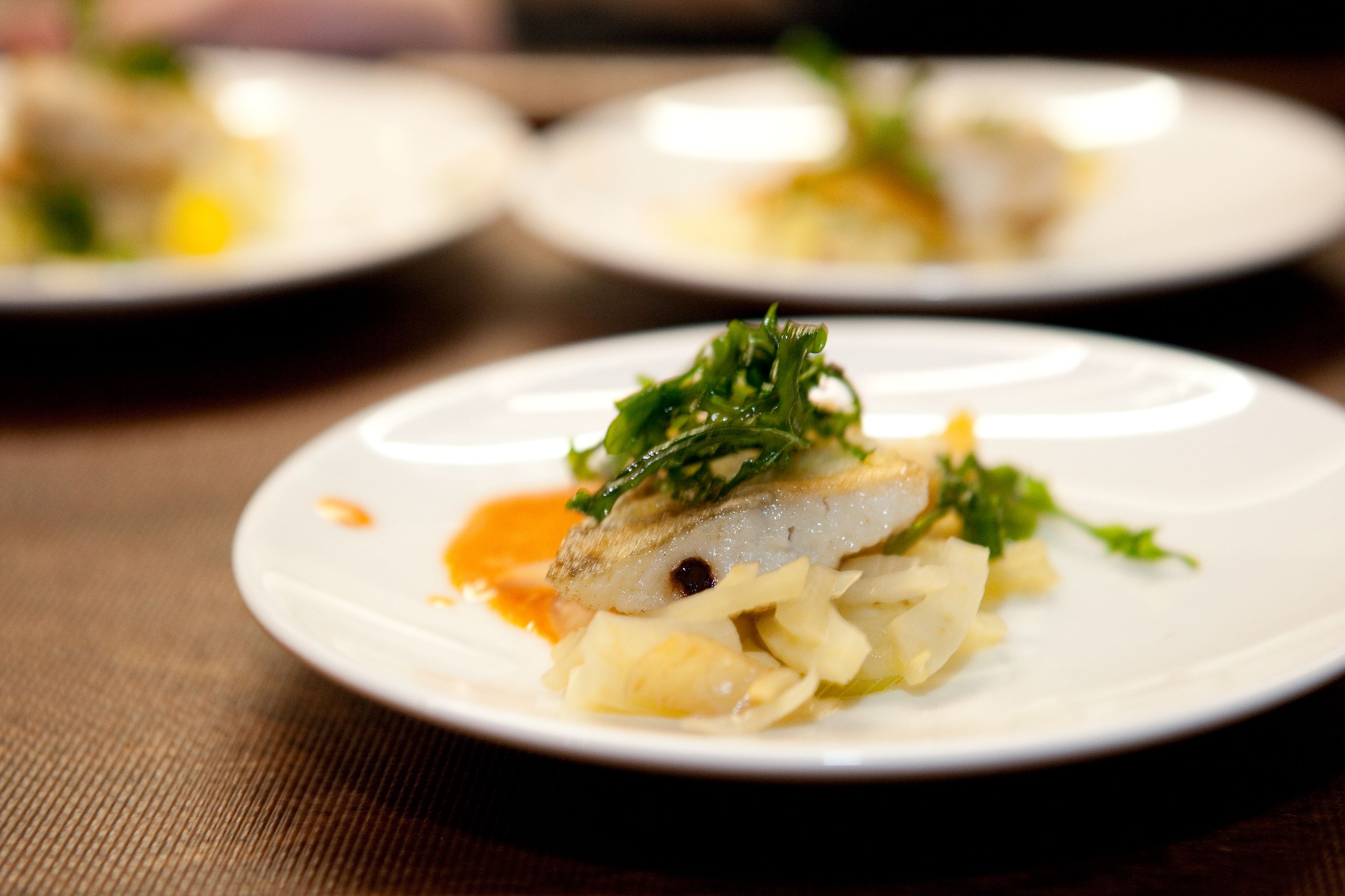 A plate of food with a piece of fish and greens on a white plate.