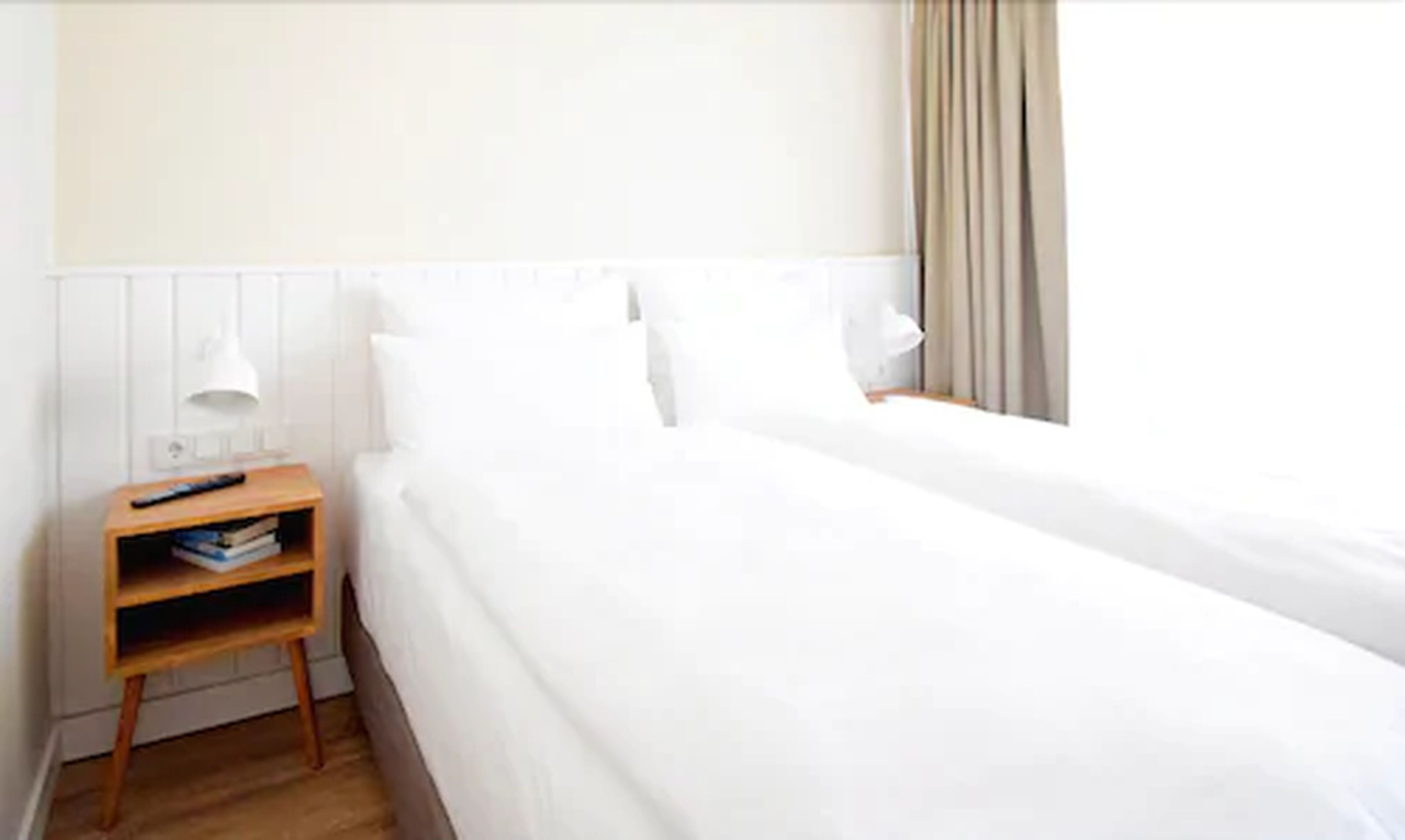 Een hotelkamer met een eenpersoonsbed, een nachtkastje met een lamp en een bijzetmeubel met boeken.