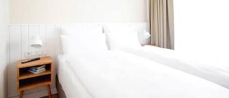 Een hotelkamer met een eenpersoonsbed, een nachtkastje met een lamp en een bijzetmeubel met boeken.