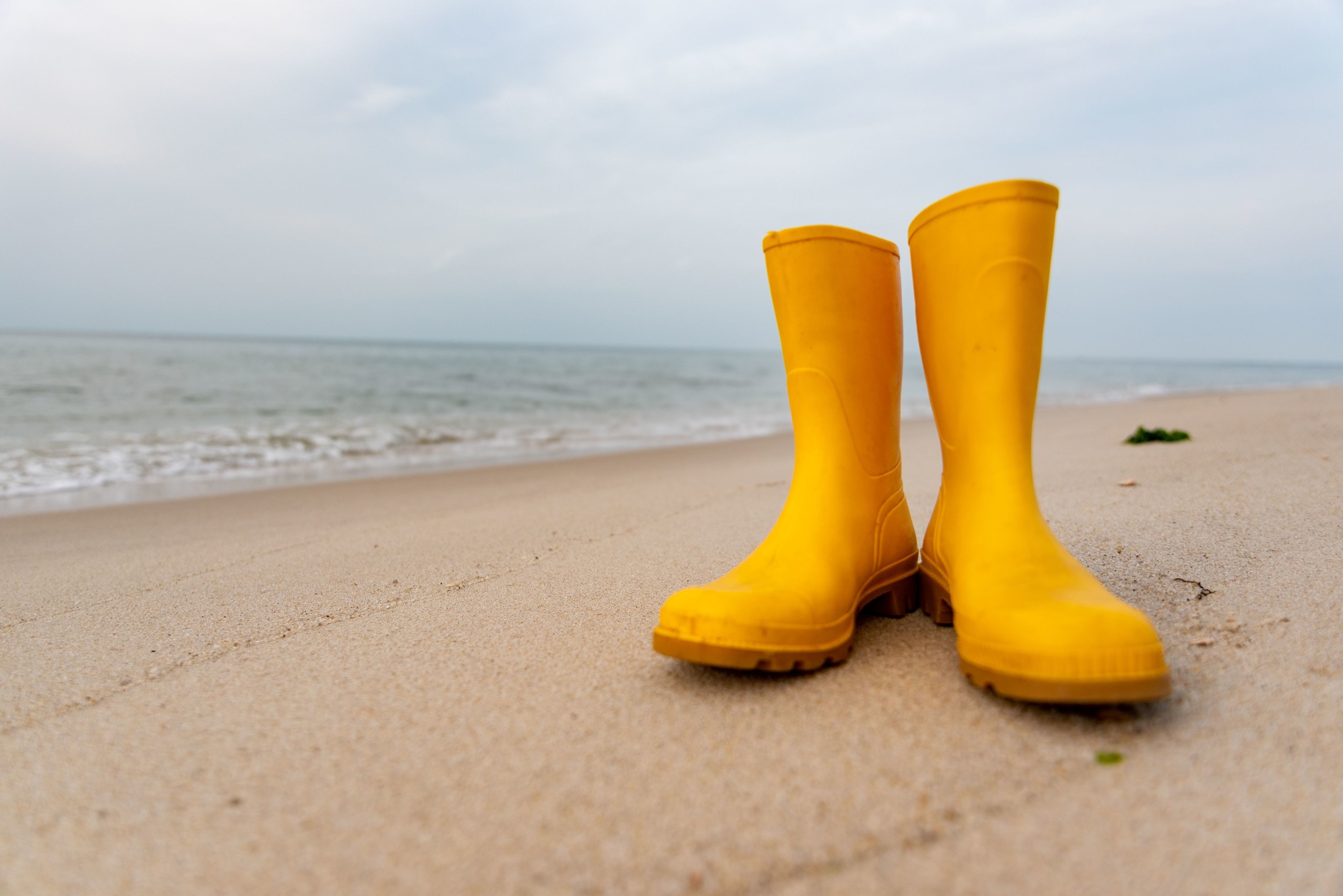 Um par de botas de borracha amarelas numa praia arenosa, com o oceano ao fundo.