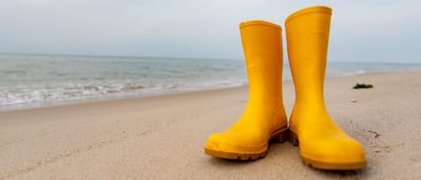 Um par de botas de borracha amarelas numa praia arenosa, com o oceano ao fundo.