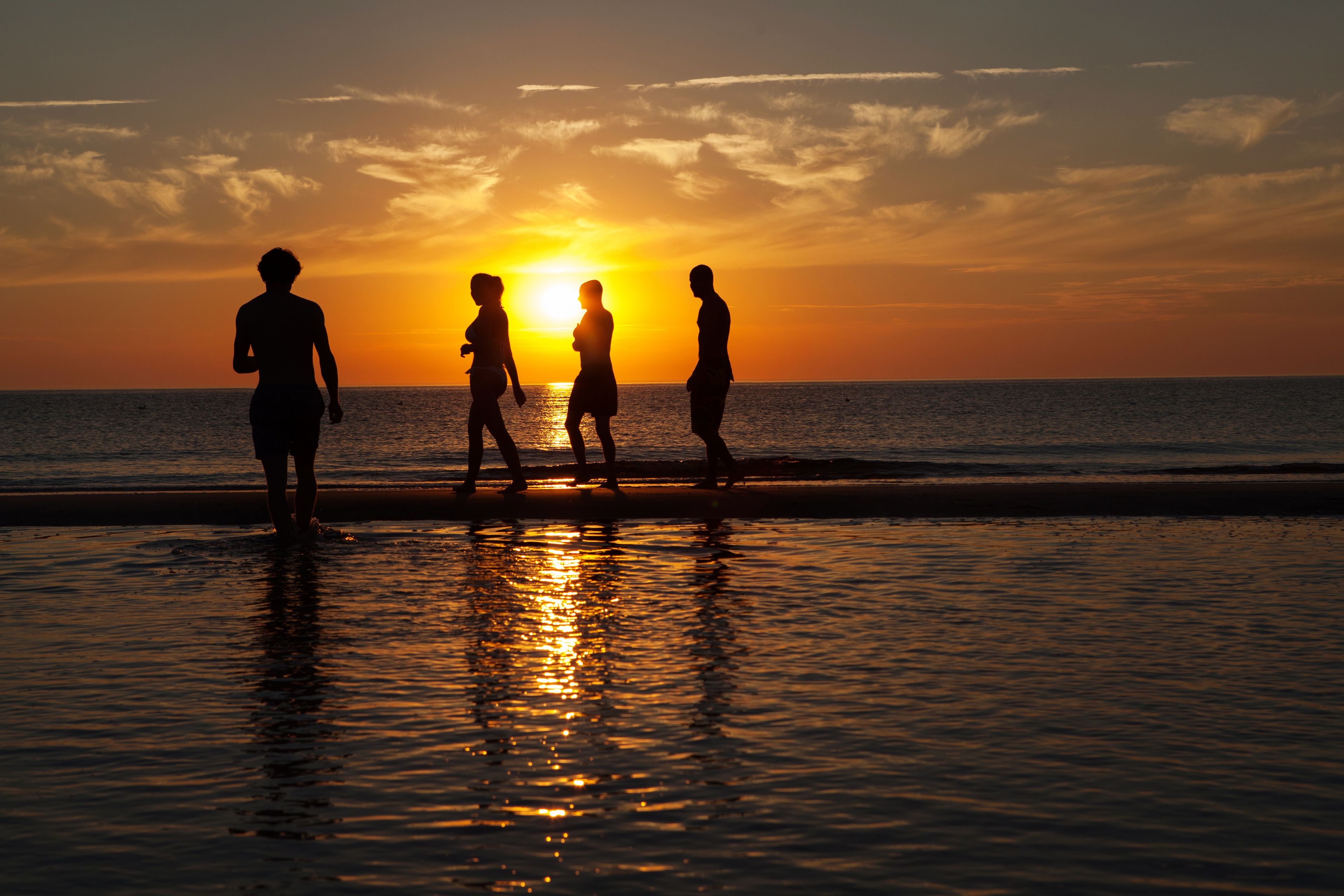 Ein Sonnenuntergang über einem Strand, Menschen laufen am Ufer entlang.