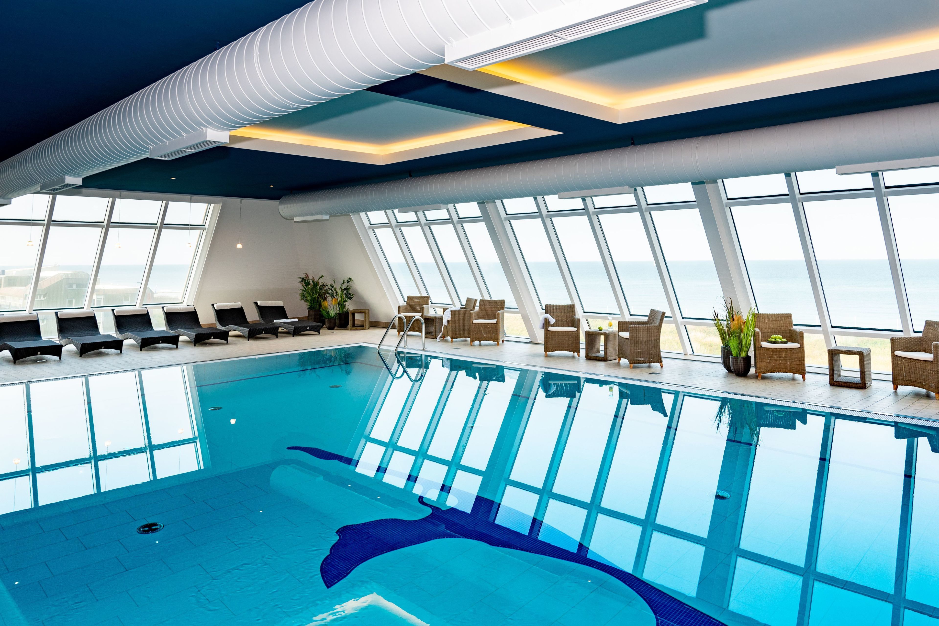 Ein moderner, überdachter Pool mit großen Glaswänden, Liegestühlen und Zimmerpflanzen.