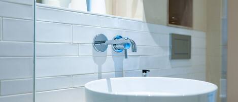 Un baño con un lavamanos blanco, un espejo y una pared de azulejos blancos.