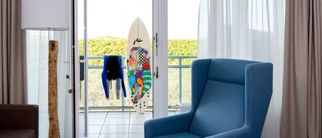 Una habitación con un sillón azul, una mesita redonda y una tabla de surf con diseños coloridos.