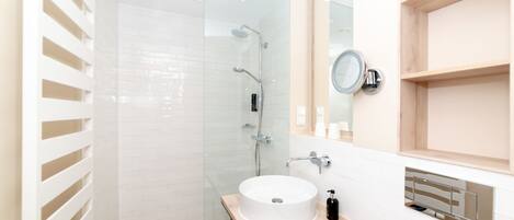 Un baño moderno con cabina de ducha de vidrio, un lavabo blanco con encimera de madera y un espejo con marco redondo.