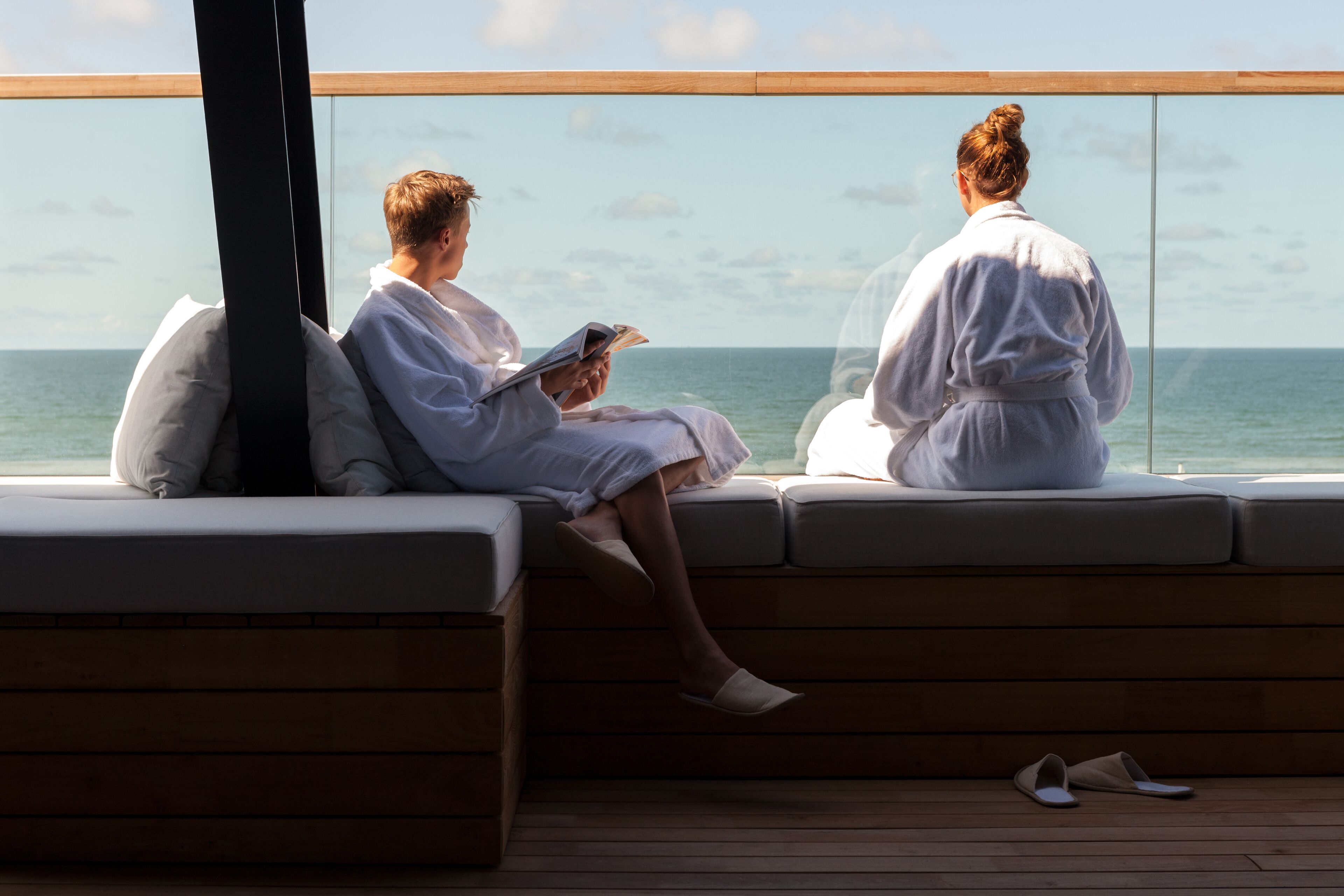 Two people sitting on a wooden deck with a view of the ocean.