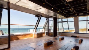 A spacious room with large windows, wooden flooring, and exercise mats arranged for physical activities.
