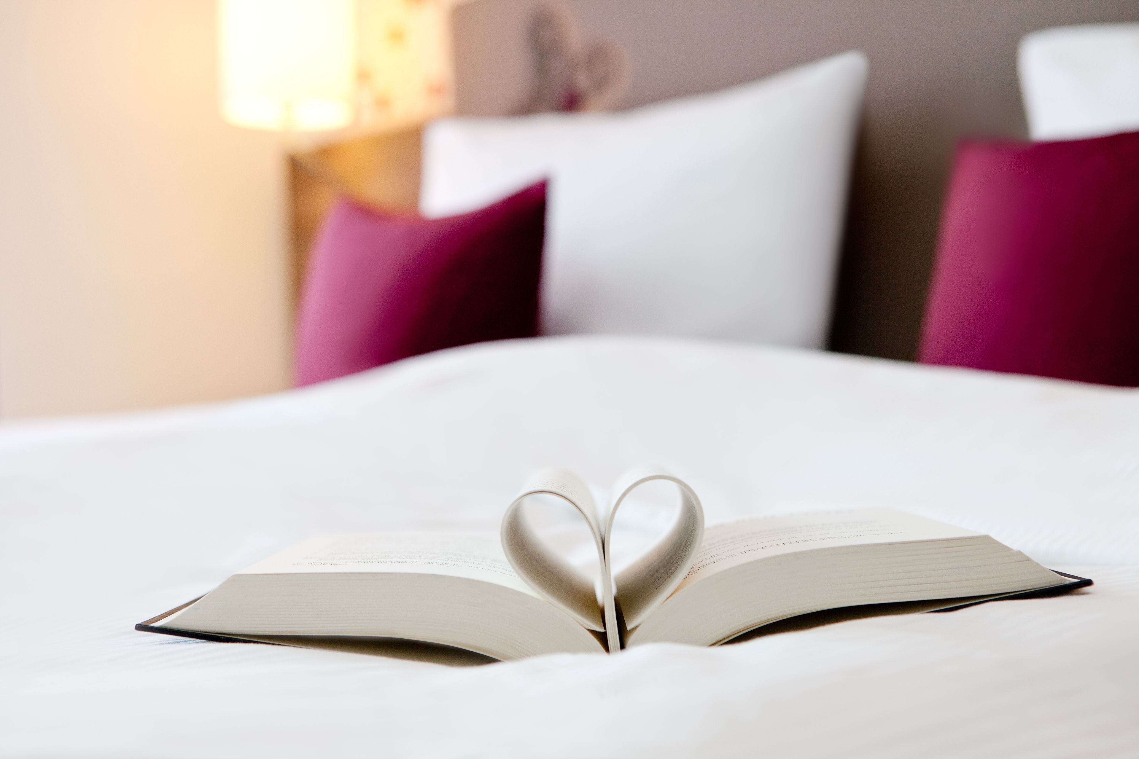 Un libro abierto con un marcapáginas con forma de corazón sobre una cama.