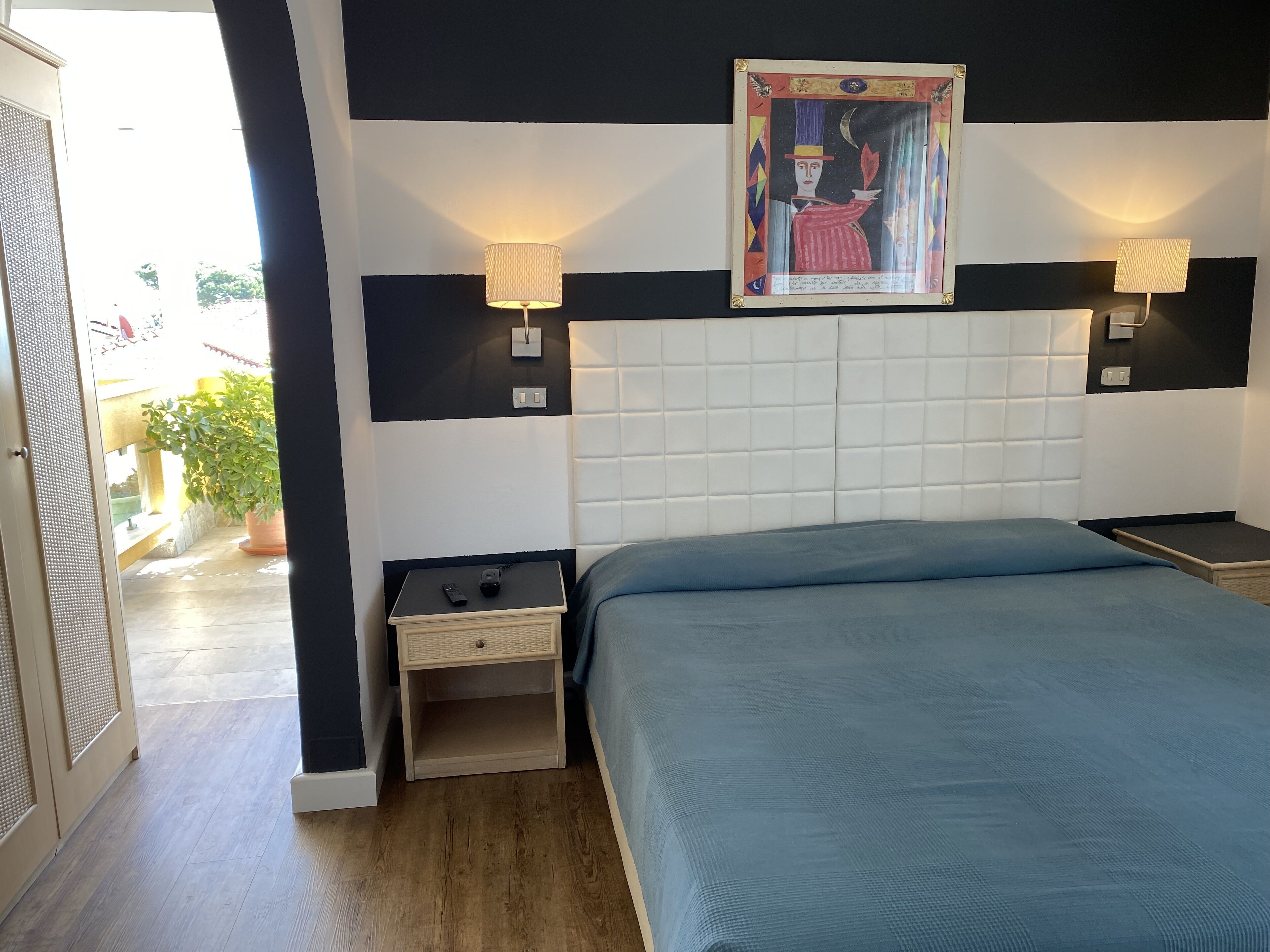 Un dormitorio con una cama grande, dos mesitas de noche, una lámpara de pared y una obra de arte enmarcada sobre la cama.