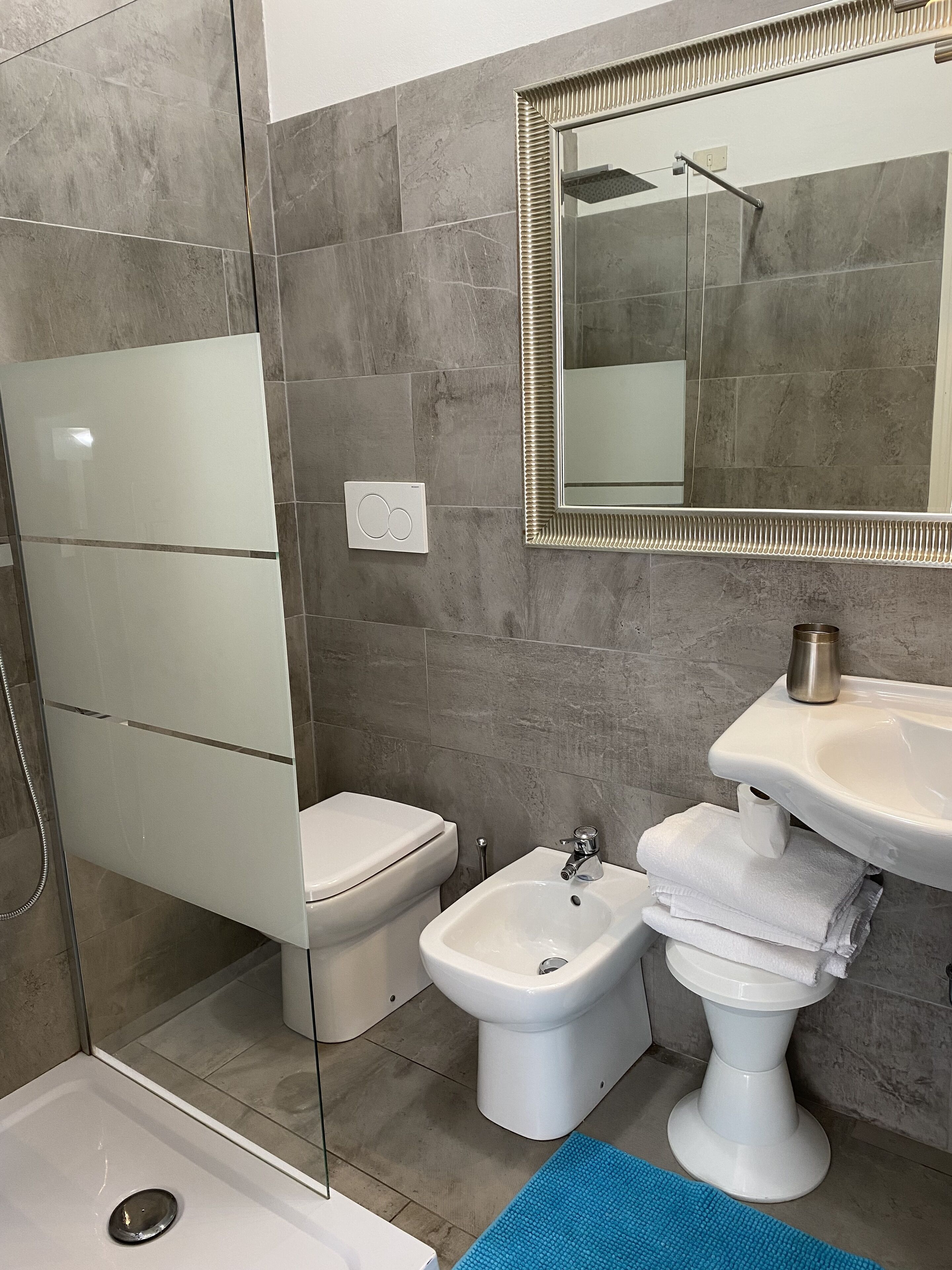 Un baño moderno con cabina de ducha de vidrio, inodoro, bidé y lavamanos con toallas apiladas.