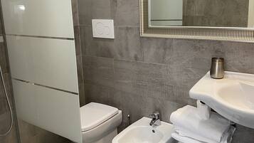 Un baño moderno con cabina de ducha de vidrio, inodoro, bidé y lavamanos con toallas apiladas.