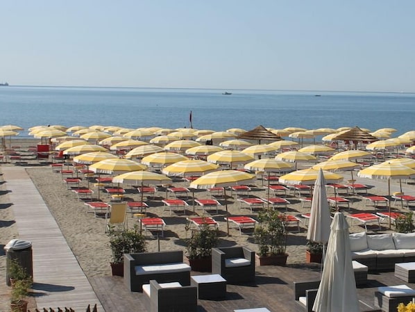 A beachside hotel with rows of sunbeds and umbrellas, a wooden walkway, and a view of the sea.