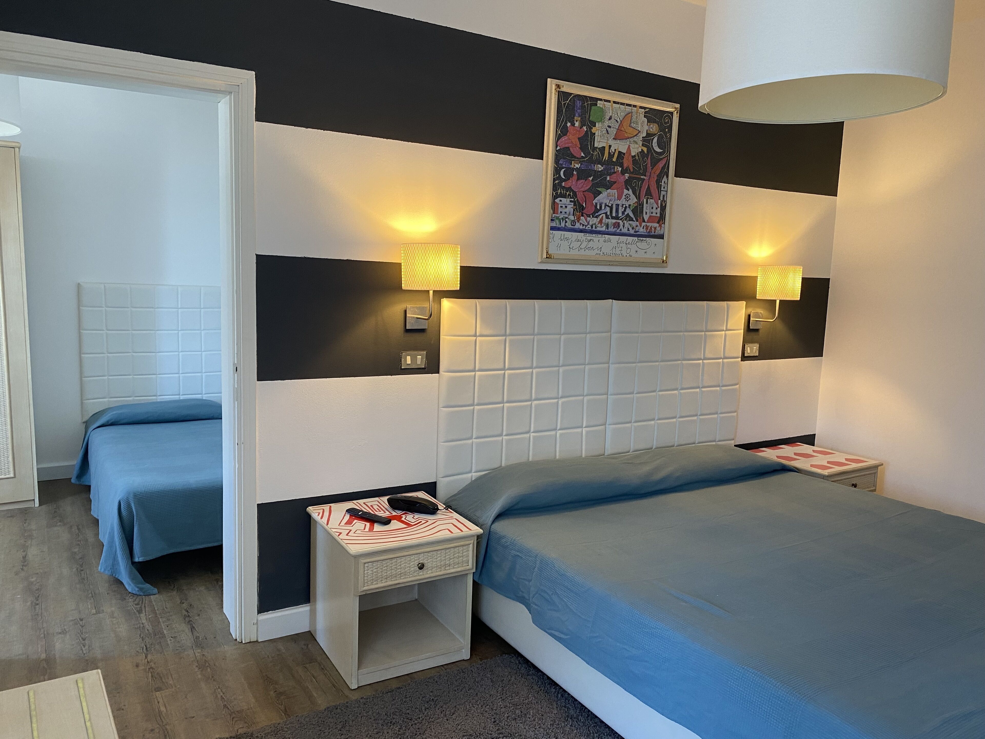 A hotel room with a large bed, two bedside tables, a headboard, and a wall-mounted artwork.