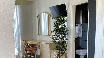 Un dormitorio con cama, escritorio, silla, planta en maceta y baño visible a través de un arco.