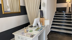 Een receptiebalie met de tekst 'BUREAU', een computer, een menukaart en een decoratief object. Een trap met zwarte treden leidt naar een ander gedeelte.